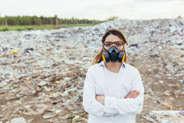 Female scientist in a protective respirator mask at a landfill assesses the level of environmental pollution